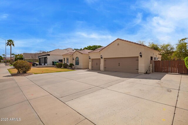 mediterranean / spanish-style house with fence, a tiled roof, concrete driveway, stucco siding, and a garage