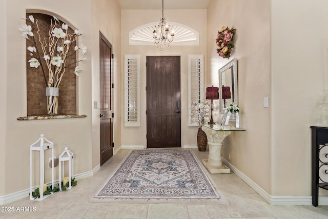 tiled entrance foyer featuring a notable chandelier and baseboards