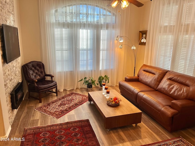 living room featuring a stone fireplace, ceiling fan, light hardwood / wood-style floors, and a healthy amount of sunlight