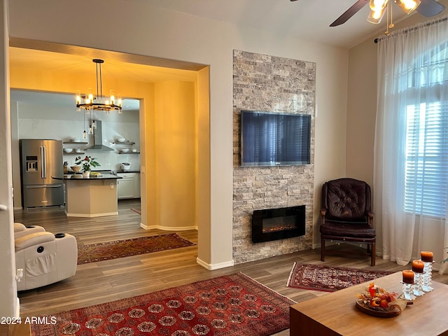 living room with a stone fireplace, dark hardwood / wood-style floors, and ceiling fan with notable chandelier