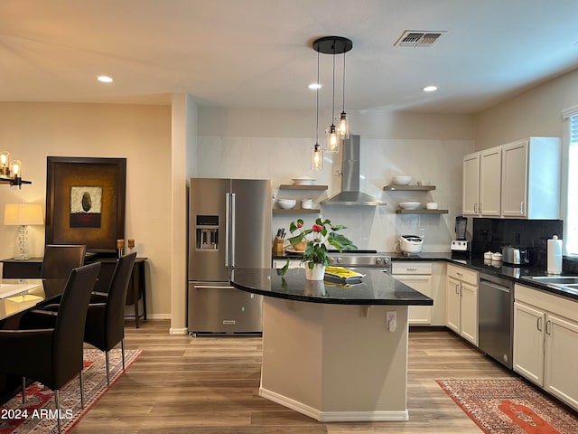 kitchen with stainless steel appliances, pendant lighting, wall chimney exhaust hood, white cabinetry, and light hardwood / wood-style flooring