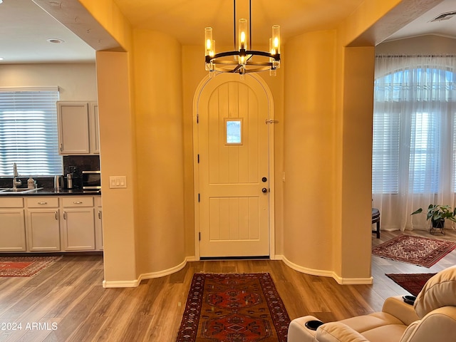 foyer entrance with hardwood / wood-style flooring, a chandelier, sink, and vaulted ceiling