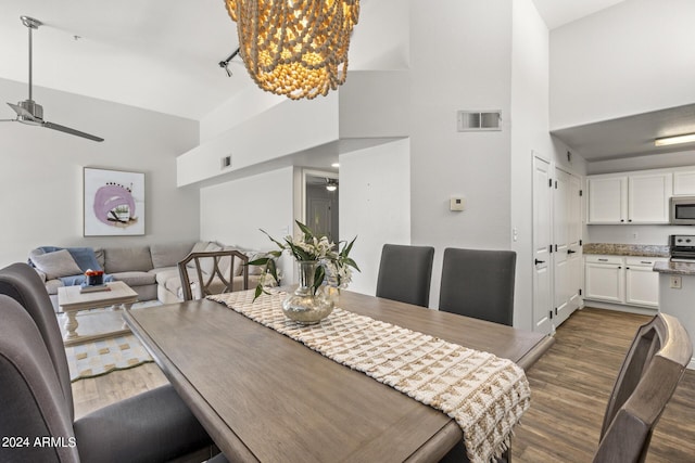 dining room featuring ceiling fan with notable chandelier, visible vents, a high ceiling, and dark wood-style floors