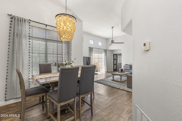 dining area with visible vents, a towering ceiling, wood finished floors, and ceiling fan with notable chandelier