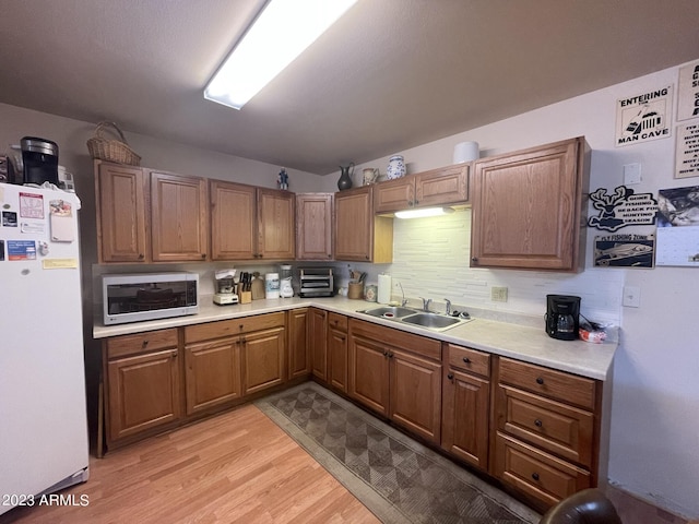 kitchen with tasteful backsplash, white fridge, sink, and light wood-type flooring