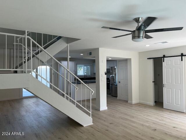 staircase with sink, a barn door, wood-type flooring, and ceiling fan