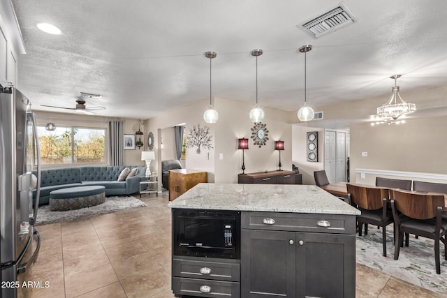 kitchen with hanging light fixtures, black microwave, stainless steel fridge, light stone counters, and ceiling fan with notable chandelier