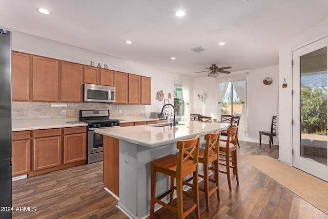 kitchen with dark hardwood / wood-style floors, a breakfast bar area, a center island with sink, sink, and appliances with stainless steel finishes