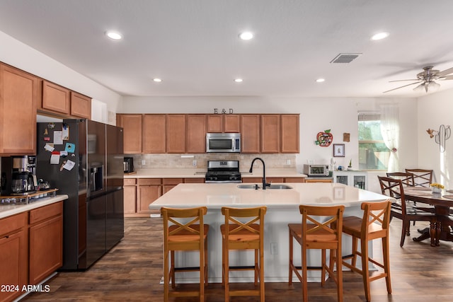 kitchen featuring decorative backsplash, dark wood-type flooring, stainless steel appliances, a center island with sink, and a breakfast bar