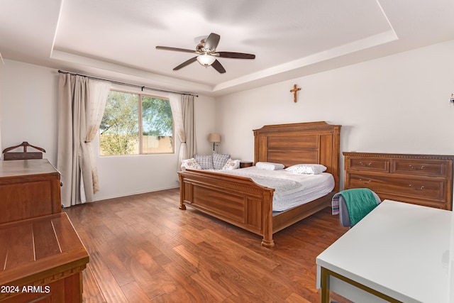 bedroom featuring ceiling fan, a tray ceiling, and dark hardwood / wood-style flooring