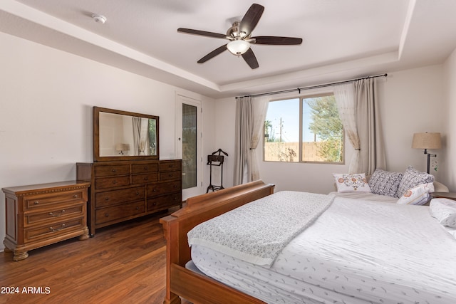 bedroom featuring a raised ceiling, dark hardwood / wood-style floors, and ceiling fan