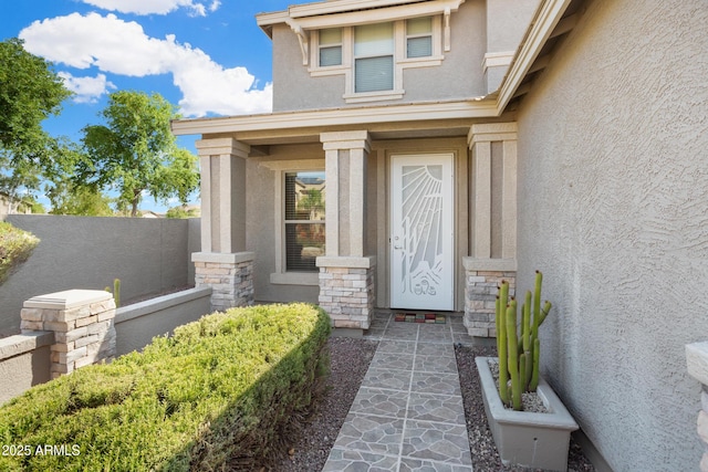 view of exterior entry featuring stone siding, fence, and stucco siding