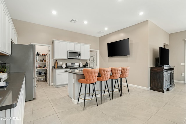 kitchen with a kitchen breakfast bar, stainless steel appliances, a kitchen island with sink, white cabinets, and light tile patterned flooring