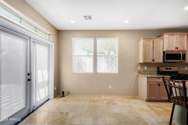 kitchen with light brown cabinetry, appliances with stainless steel finishes, and light stone countertops