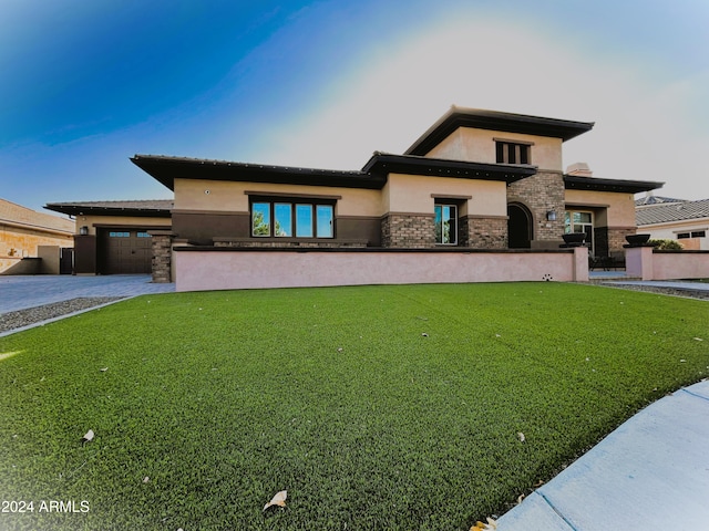 prairie-style home featuring stucco siding, driveway, stone siding, an attached garage, and a front yard