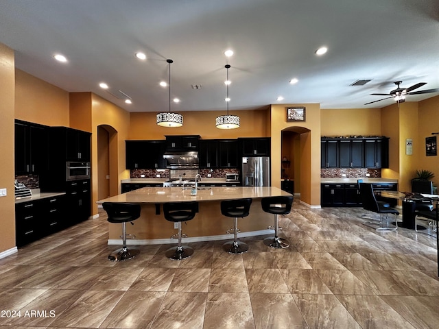 kitchen featuring a center island with sink, hanging light fixtures, decorative backsplash, ceiling fan, and stainless steel fridge with ice dispenser