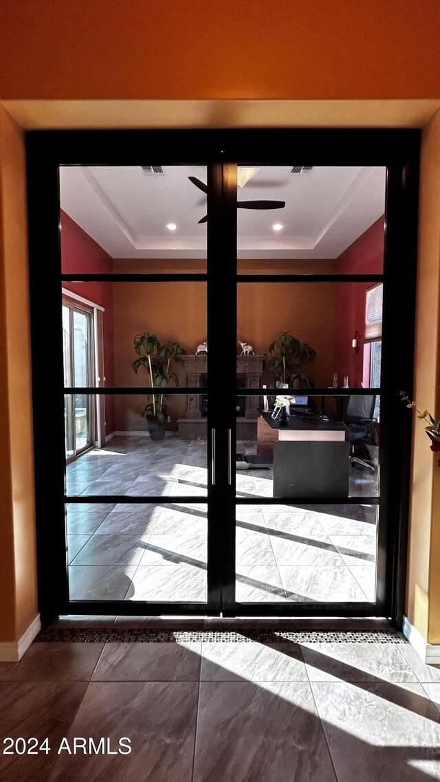 doorway to outside featuring a raised ceiling, ceiling fan, and tile patterned flooring