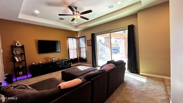 carpeted living room with a tray ceiling and ceiling fan