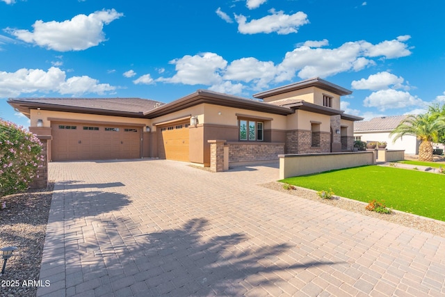 prairie-style house with a front lawn, decorative driveway, a garage, and stucco siding