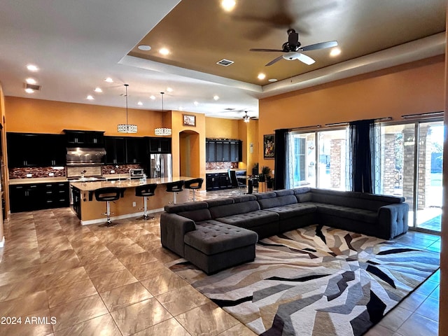 living room featuring ceiling fan, a towering ceiling, and a tray ceiling