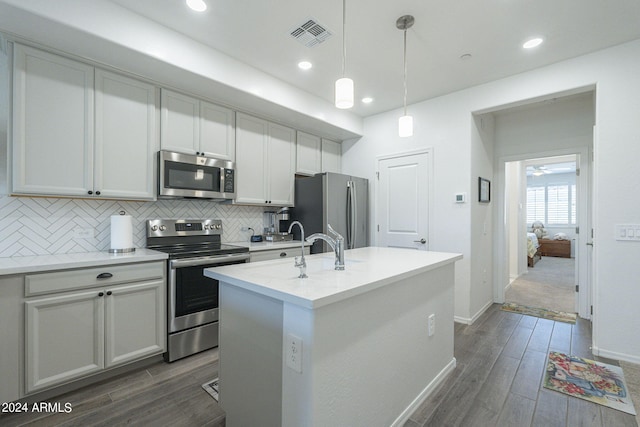 kitchen featuring backsplash, dark hardwood / wood-style flooring, hanging light fixtures, appliances with stainless steel finishes, and a center island with sink