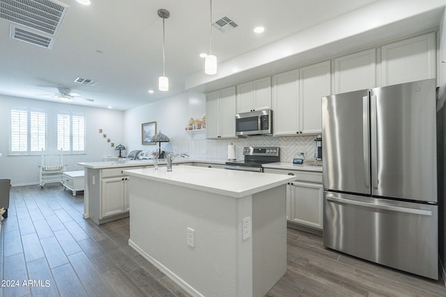 kitchen with decorative light fixtures, appliances with stainless steel finishes, dark wood-type flooring, ceiling fan, and a center island with sink