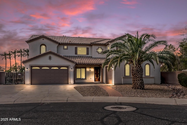 mediterranean / spanish-style house with stucco siding, driveway, a tile roof, fence, and an attached garage