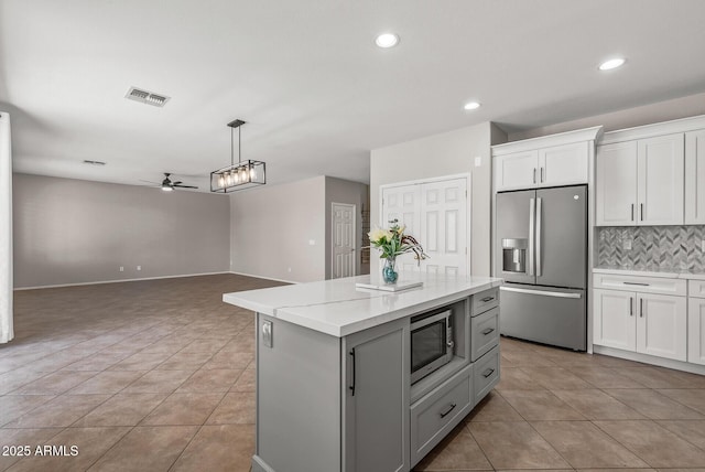 kitchen with backsplash, light tile patterned floors, appliances with stainless steel finishes, white cabinetry, and a ceiling fan