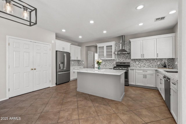 kitchen featuring visible vents, a kitchen island, appliances with stainless steel finishes, white cabinets, and wall chimney exhaust hood