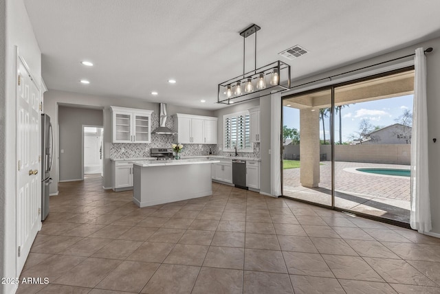 kitchen with visible vents, backsplash, wall chimney range hood, light countertops, and stainless steel appliances