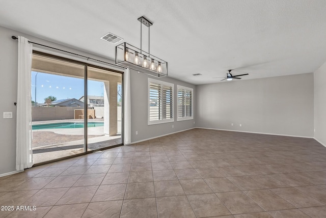 tiled empty room with visible vents, baseboards, and ceiling fan