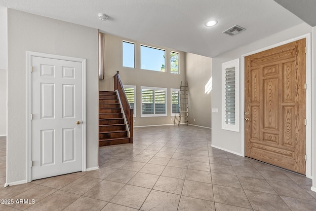 foyer entrance with light tile patterned flooring, visible vents, stairs, and baseboards