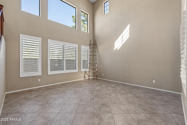 unfurnished living room featuring tile patterned flooring, baseboards, and a towering ceiling