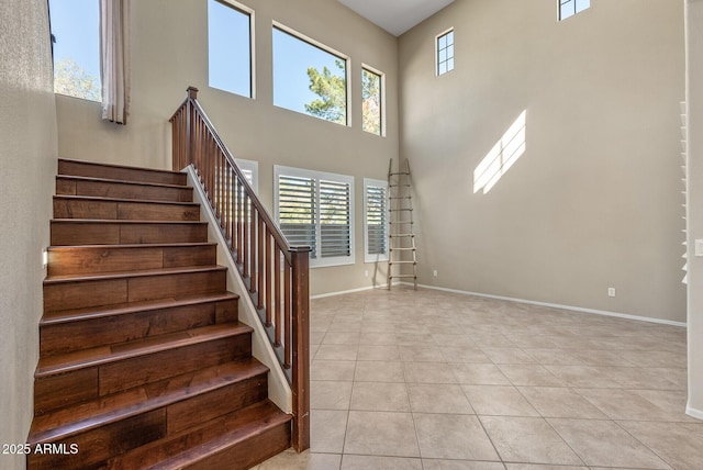 stairway with tile patterned floors, plenty of natural light, baseboards, and a towering ceiling