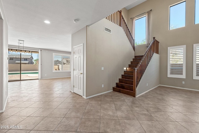 interior space with tile patterned flooring, visible vents, a high ceiling, and baseboards