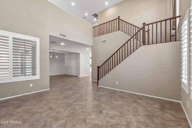 unfurnished living room with visible vents, stairs, and a high ceiling