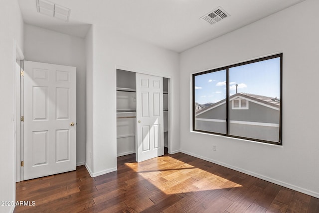 unfurnished bedroom with dark wood finished floors, visible vents, and a closet