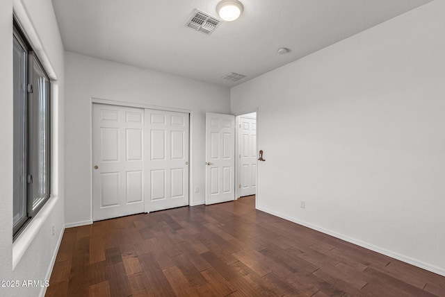 unfurnished bedroom featuring visible vents, baseboards, a closet, and dark wood-style flooring