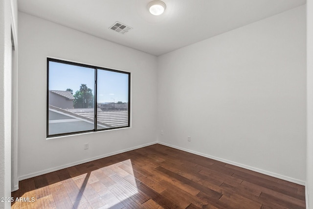 spare room featuring visible vents, baseboards, and dark wood-type flooring