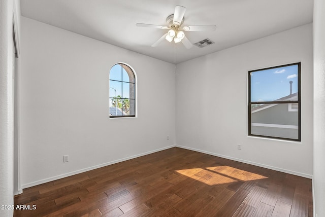 spare room with baseboards, dark wood-style floors, visible vents, and ceiling fan