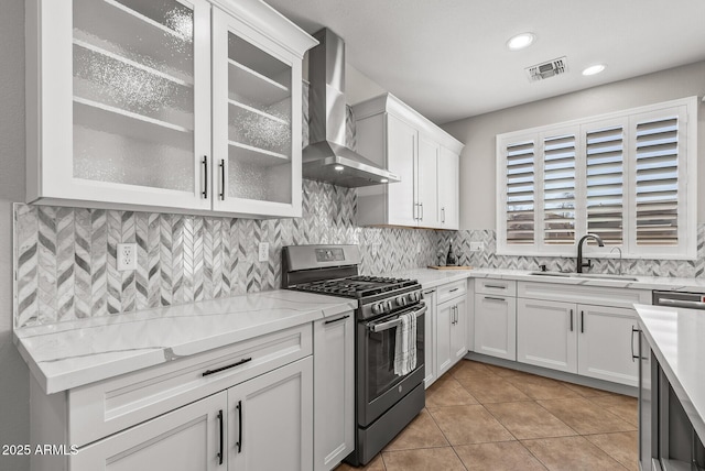 kitchen featuring visible vents, stainless steel range with gas cooktop, a sink, wall chimney range hood, and tasteful backsplash