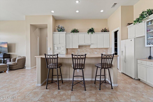 kitchen with white appliances, tasteful backsplash, a breakfast bar, and white cabinets