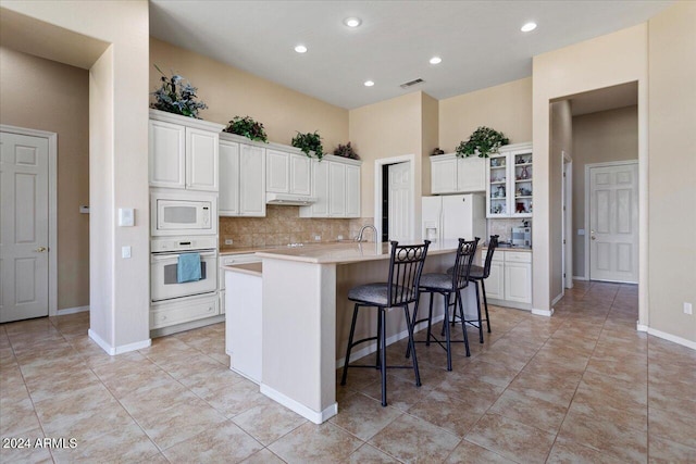 kitchen featuring white cabinets, backsplash, an island with sink, a breakfast bar, and white appliances