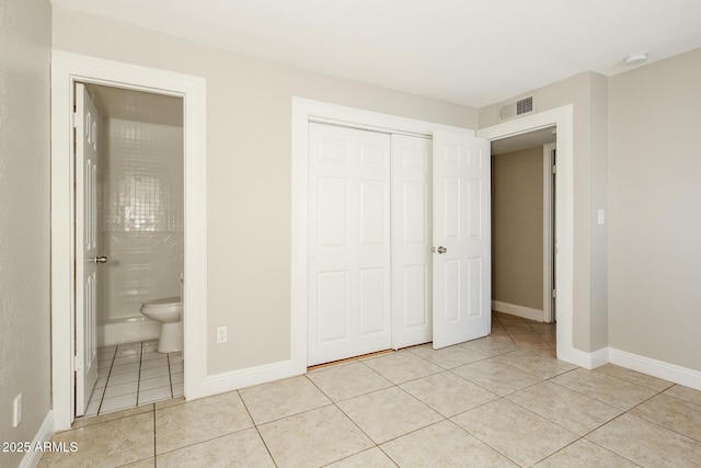 unfurnished bedroom with light tile patterned floors, a closet, and ensuite bathroom