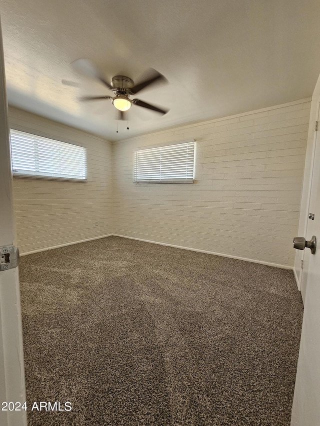 carpeted spare room with ceiling fan and brick wall