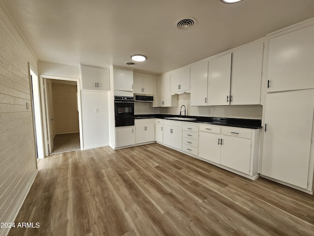 kitchen with sink, black oven, light hardwood / wood-style flooring, white cabinetry, and range hood