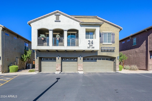 view of property featuring an attached garage, stucco siding, central air condition unit, a balcony, and driveway