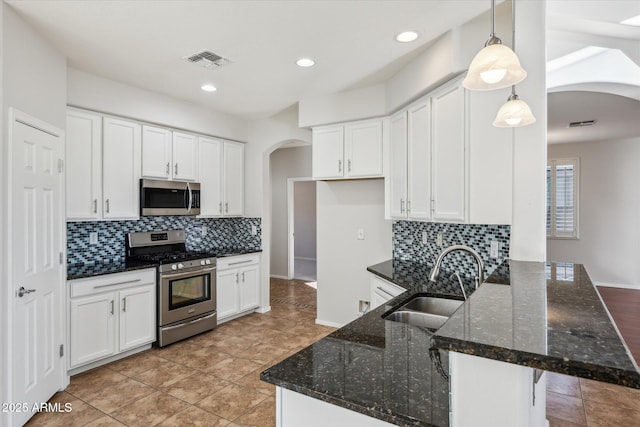 kitchen featuring sink, hanging light fixtures, stainless steel appliances, dark stone counters, and white cabinets