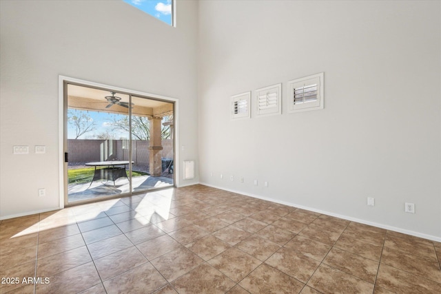 tiled empty room with ceiling fan and a high ceiling