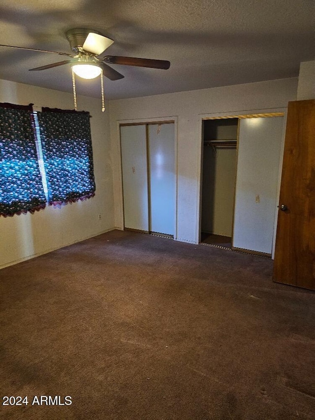 unfurnished bedroom featuring a textured ceiling, carpet floors, two closets, and ceiling fan